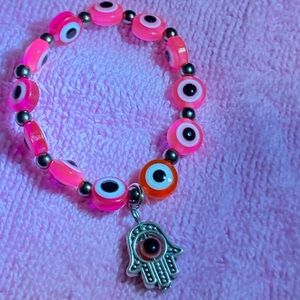 The color is Pink The design includes a hand charm abs a evil eye charm